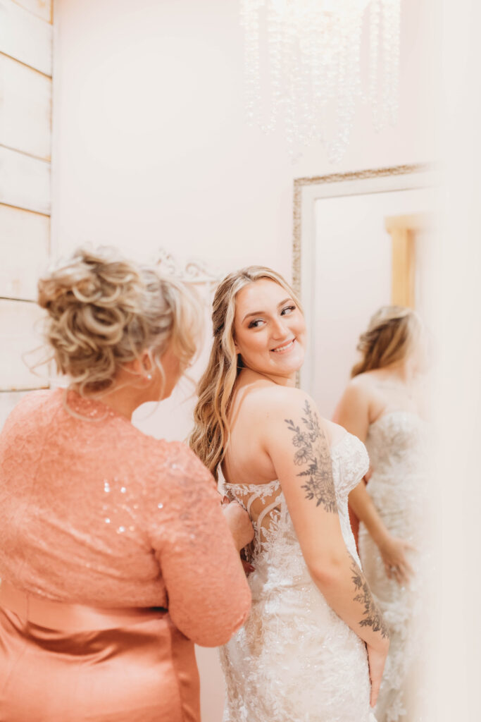 Mother in peach dress zips up the back of her daughter's wedding dress in Princeton, WV. 