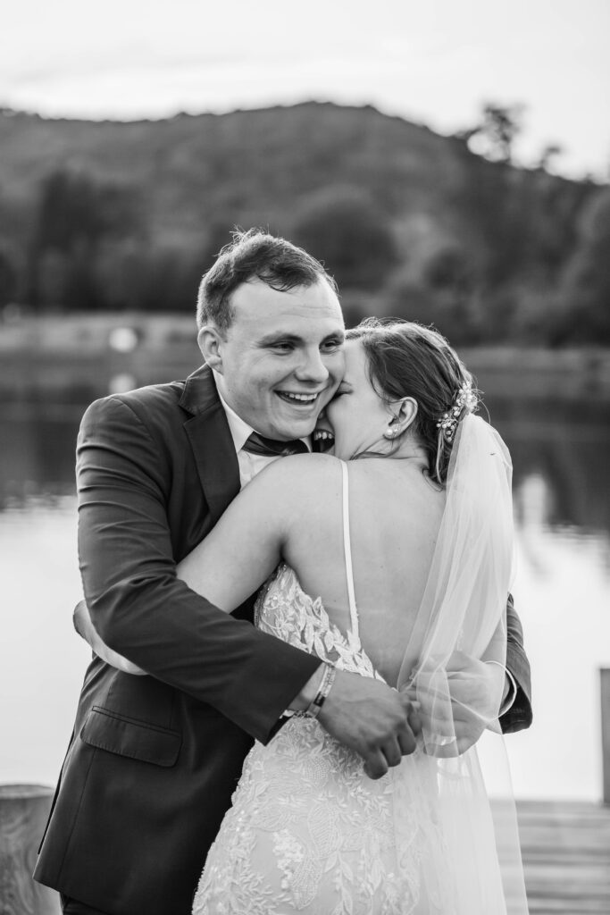 A bride and groom embrace in a huge and laugh together by the water at Lake Mountain Manor in Princeton, West Virginia. 