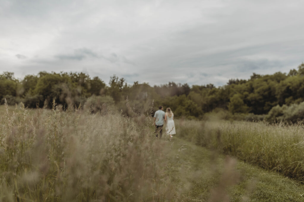 A woman and man walk away and the camera focuses on weeds during an engagement photos at Heritage Community Park in Blacksburg, Virginia.