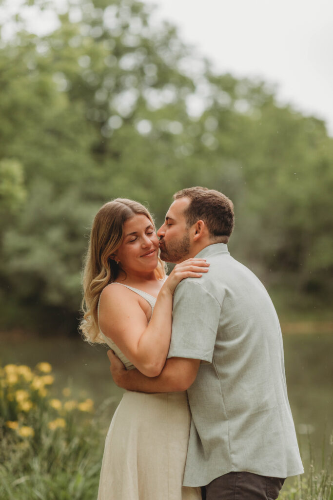 A man kisses a woman's cheek during engagement photos at Heritage Community Park in Blacksburg, Virginia with yellow flowers around them.