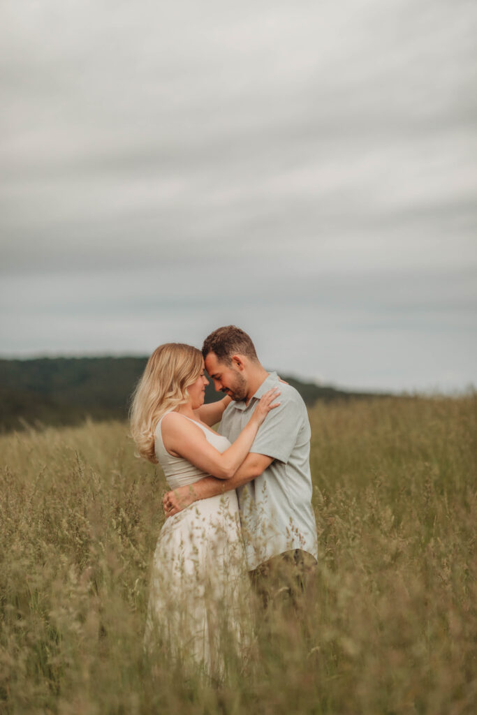 A woman and man embrace in a field at Heritage Community park during engagement photos in Blacksburg, Virginia