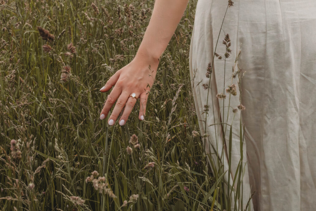A woman touches the grass and shows off her ring during engagement photos in Blacksburg, Virginia.