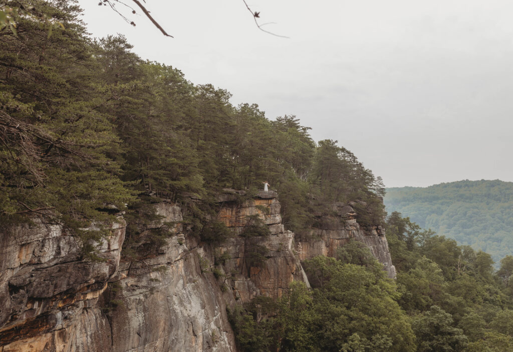 A wide angled photo of a couple dancing together on a cliff at the New River Gorge.