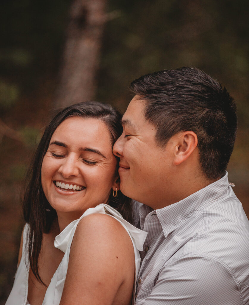 A man presses his nose into a woman's temple while they laugh together.