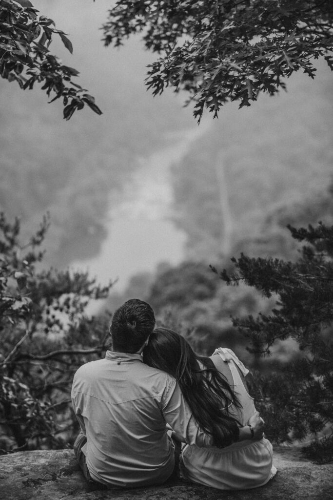A couple hug and stare at the New River at the New River Gorge during engagement photos.