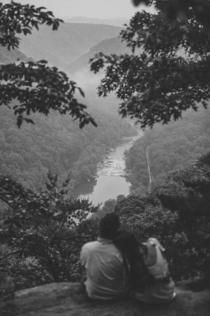 A couple lean on each other and look at the view during New River Gorge engagement photos.