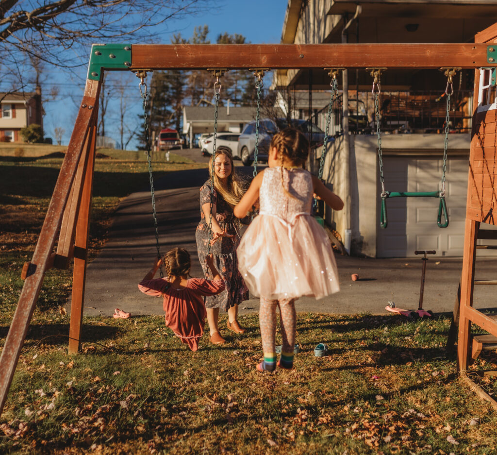 A mother is pushing her children on the swings outside of their home during an in home documentary session.
