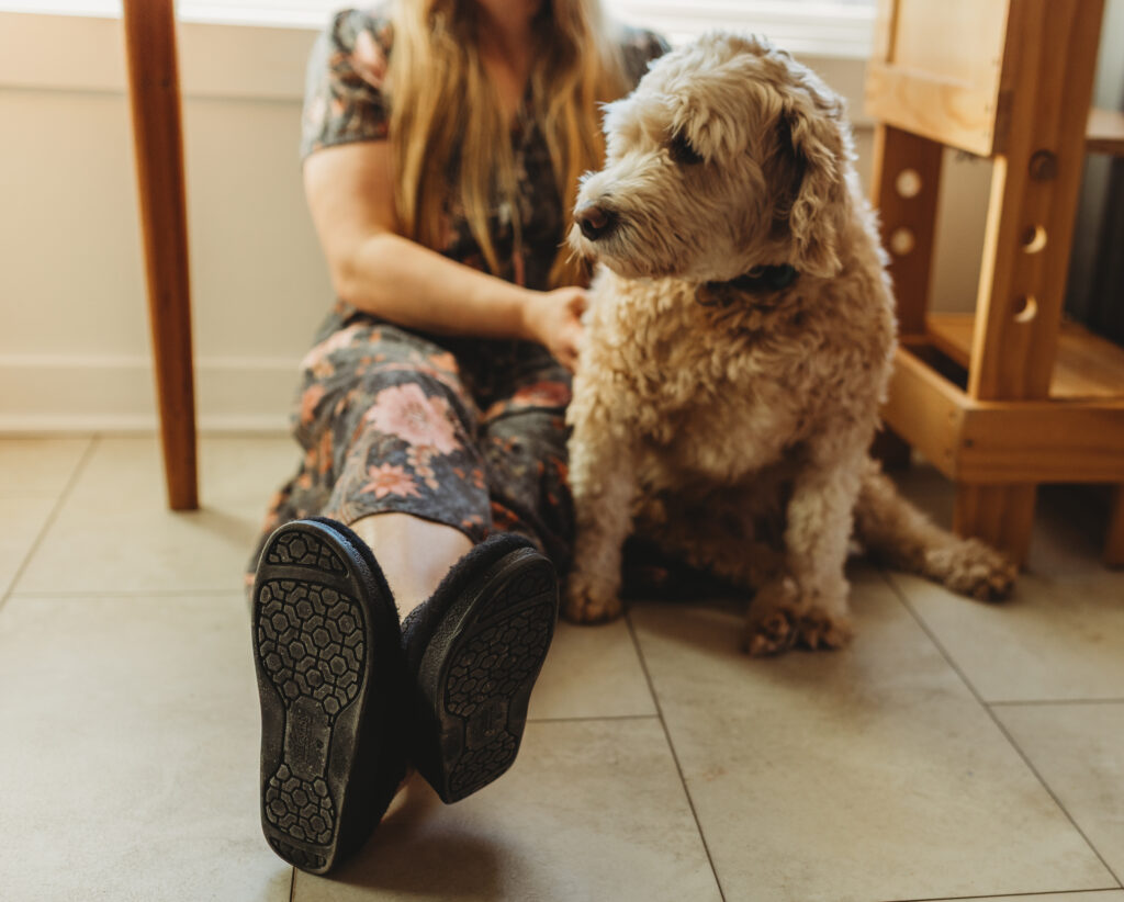 A woman with slippers on is seen in the floor with her shaggy dog during in home documentary photos.