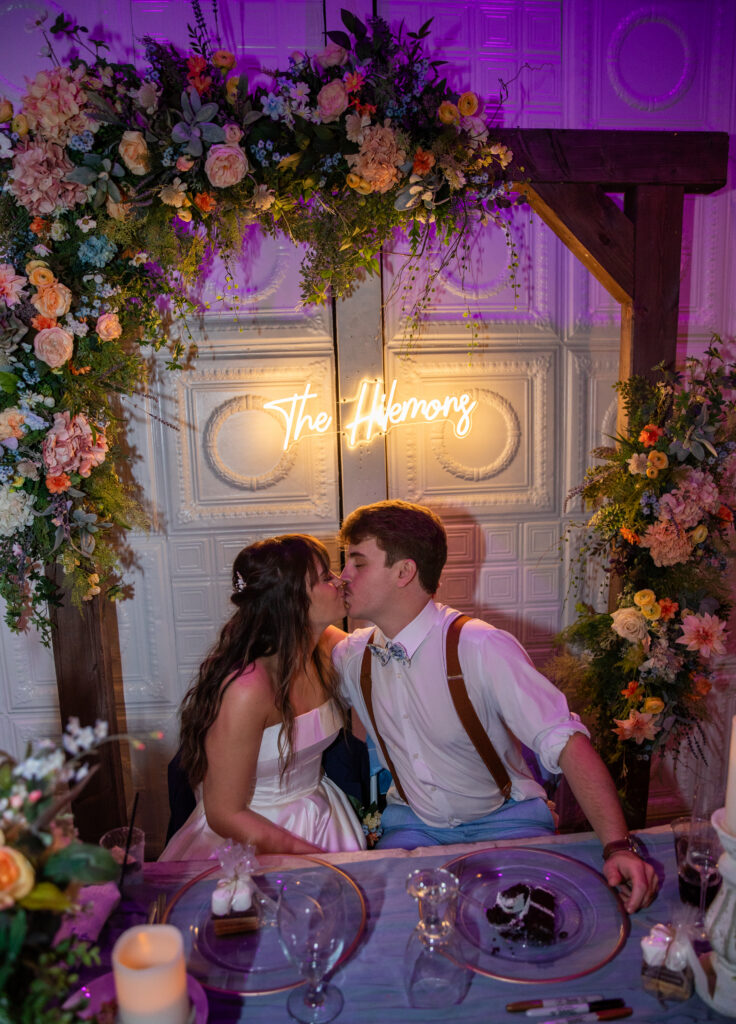 The bride and groom kiss under their wedding sign that reads "The Hilemons"