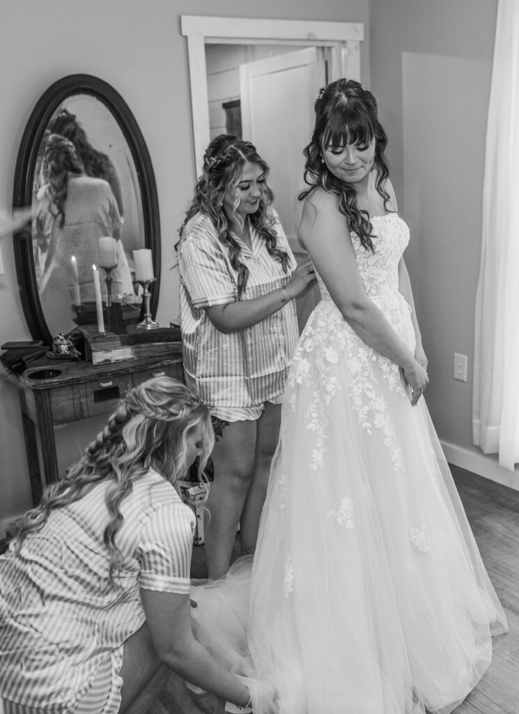 Bridesmaids zipping bride up at a Vintage Valley Wedding. 